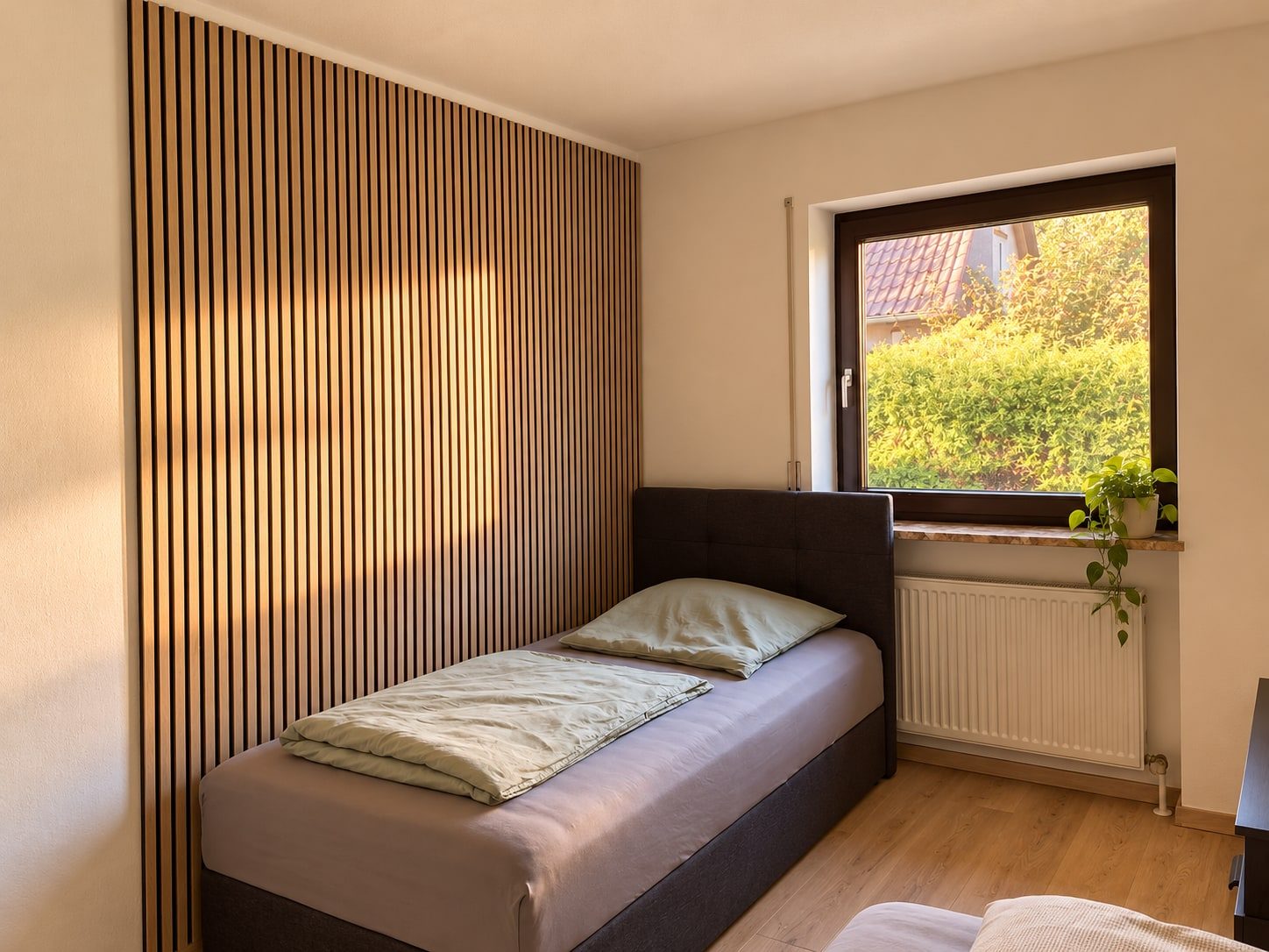 Zweibettzimmer mit Einzelbett, Holzlamellenwand und Fenster mit Blick auf die Hecke